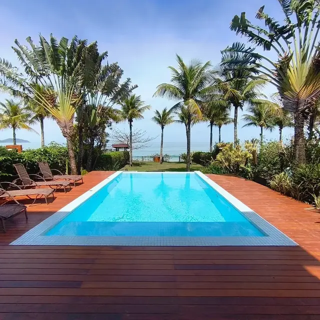 Piscina com deque de madeira, espreguiçadeiras e vista para o mar entre coqueiros