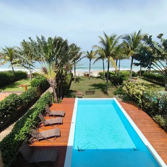 Vista aérea da piscina com deque de madeira, jardim e a praia ao fundo